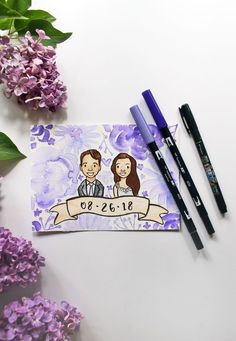 two pens are sitting on top of a notepad next to some flowers and purple lilacs