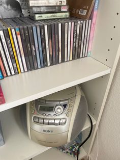 a cd player sitting on top of a white shelf next to a bunch of dvds