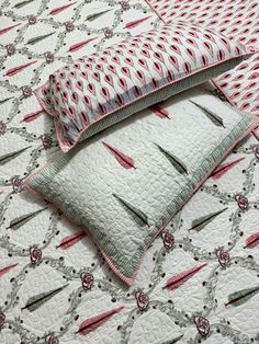 two pillows on top of a quilted bed with red and green designs in the background