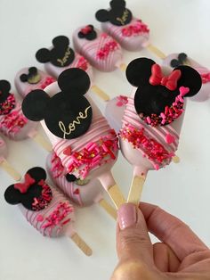 a hand holding a mickey mouse lollipop with pink sprinkles