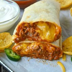 two burritos sitting on top of a tray with chips and salsa in the background