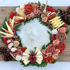 a christmas wreath made out of apples, pine cones and other holiday decorations on a wooden surface