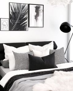 a black and white bedroom with lots of pillows on the bed, pictures above it