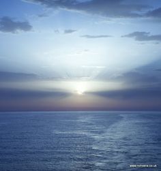 the sun is setting over the ocean with clouds in the sky and water below it