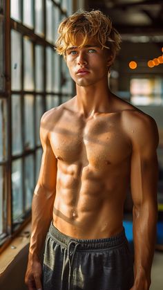 a shirtless young man standing in front of a window looking at the camera with no shirt on