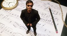 a man standing in front of sheet music with a clock and pen on top of it