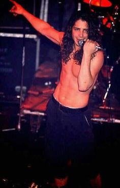 a shirtless man with long hair holding a microphone