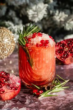 a pomegranate and rosemary garnish in a glass with ice on the table