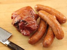 several sausages on a wooden cutting board with a knife next to them and a piece of meat in the middle