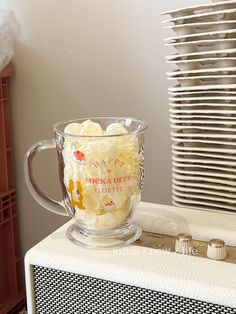 a glass mug filled with whipped cream sitting on top of a table next to stacks of plates