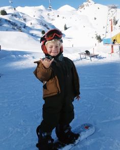 a young boy standing on top of a snow covered slope wearing skis and goggles