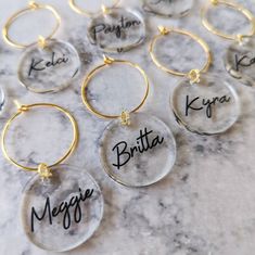 six personalized glass hoop earrings with names in black and gold on a marble surface