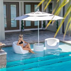 a woman sitting in a chair next to a pool with an umbrella over her head