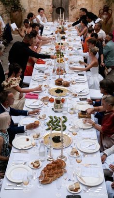 a long table with many people sitting at it and plates on the table are full of food