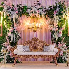 a couch sitting under a chandelier covered in flowers and greenery next to candles