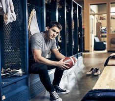 a man holding a football sitting on top of a wooden bench in front of lockers