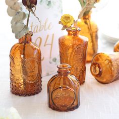 three brown glass vases with flowers in them on a white tableclothed table