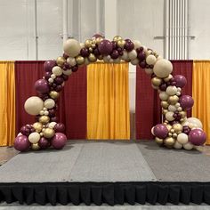 an arch made out of balloons on top of a carpeted floor in front of red and yellow drapes