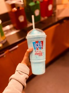 a person holding up a blue cup with ice cream on the top and a straw in it