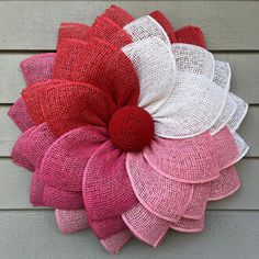 a red, white and pink flower is hanging on the side of a house wall