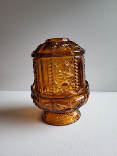 an ornate glass vase sitting on top of a white tableclothed surface, with the lid partially closed