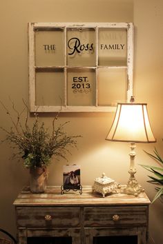 an old window is hung above a table with a lamp on it and a vase filled with flowers