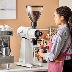 a woman standing in front of a coffee grinder with lots of beans on it