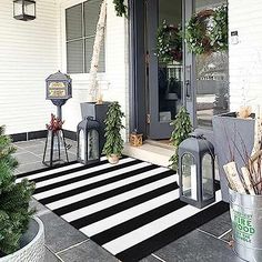 front porch decorated for christmas with black and white striped rug, potted evergreens