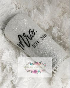 the glitter tumbler is sitting on a fluffy white blanket with black writing and flowers