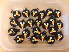 a plastic container filled with lots of black cookies covered in frosting and decorated like birds