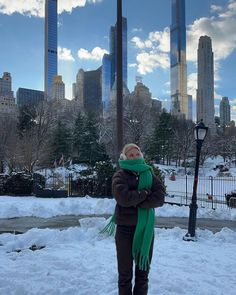 a woman is standing in the snow with her arms crossed and wearing a green scarf