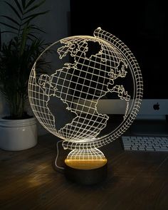 an illuminated globe sitting on top of a wooden desk next to a computer monitor and keyboard