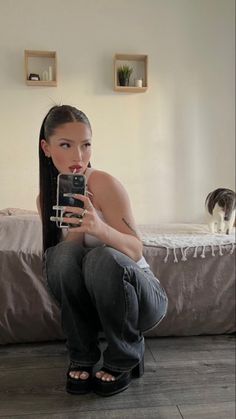 a woman is taking a selfie with her cell phone and a cat on the bed in the background