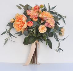 a bouquet of orange and pink flowers on a white surface with greenery around it