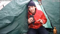 a man sitting in front of a tent holding a microphone and looking at the camera