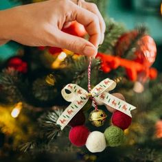 a hand holding a christmas ornament on top of a tree with ornaments hanging from it