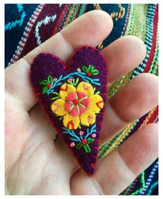 a hand holding a purple heart with yellow and red flowers