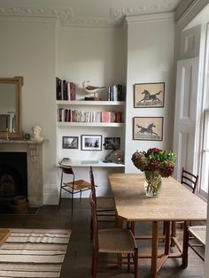 a dining room table and chairs with bookshelves on the wall in front of it