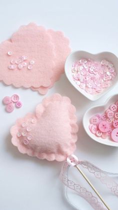 some pink buttons are sitting in bowls and on the table next to two spoons