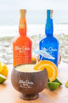 two bottles of blue chai and an orange slice sit on a table next to the ocean