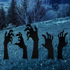 silhouettes of hands reaching up into the air in front of trees and mountains at night