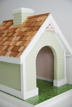 a small dog house with a roof made out of wood shingles and green grass