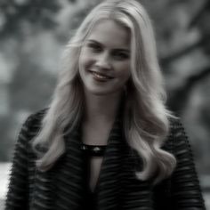 a woman with long blonde hair smiling at the camera while wearing a black and white striped jacket