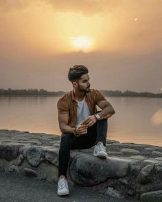 a man sitting on the edge of a rock wall next to a body of water