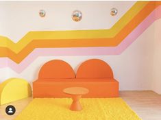 an orange couch sitting on top of a yellow rug in front of a colorful wall