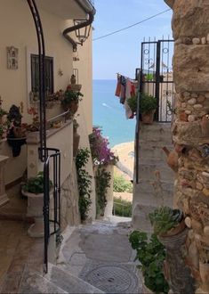 an alley way leading to the beach with potted plants and towels hanging on clothesline