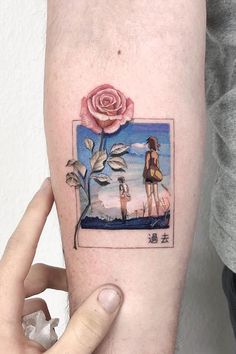 a person holding up a small tattoo with a rose on the left side of their arm