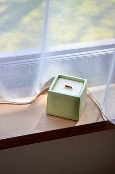 a small square box sitting on top of a window sill next to a curtain