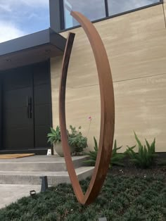 a sculpture in front of a building with grass and plants on the ground next to it