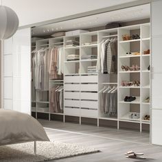 a white closet with lots of clothes and shoes on shelves next to a large bed